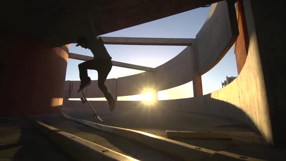 Silhouette of a young man skateboarding down a spiral ramp in a parking garage at sunset. alt