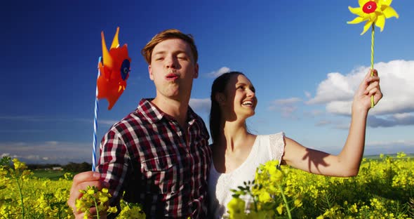 Romantic couple blowing pinwheel in mustard field alt