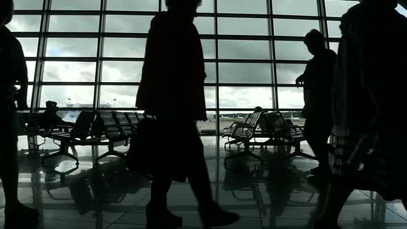 Travelers Walking Along Window in Airport Terminal, People Silhouettes Walking. alt