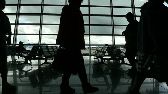 Travelers Walking Along Window in Airport Terminal, People Silhouettes Walking.