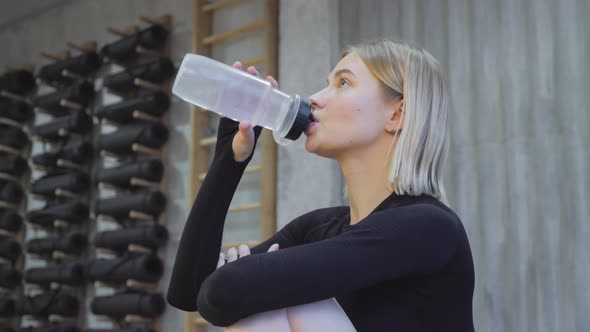 fitness girl drinking from sport bottle during a workout pause at home or gym. Close backlit alt