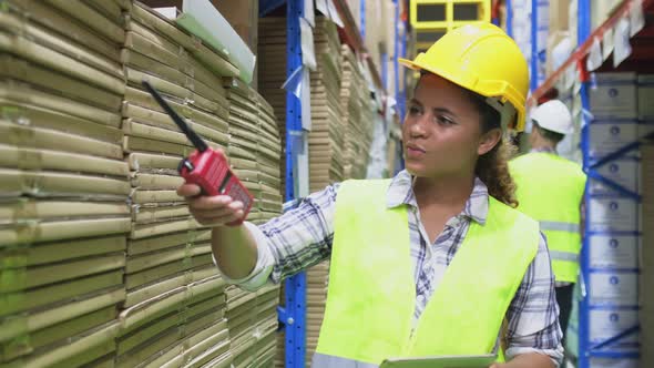 Young smiling black woman worker wear helmet and vest check box in stock in clean factory warehouse. alt