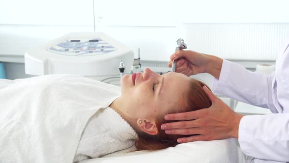 Cosmetologist Using Some Equipment on Client's Face alt