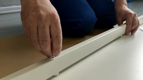 A Man a Handyman in a Blue Jumpsuit is Assembling a Table in Closeup alt