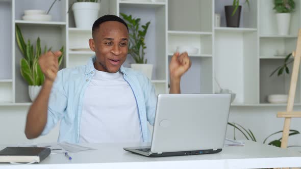 African-American Feels Happy Received Great News By Internet Looks at Pc Screen Raised Hands Scream alt