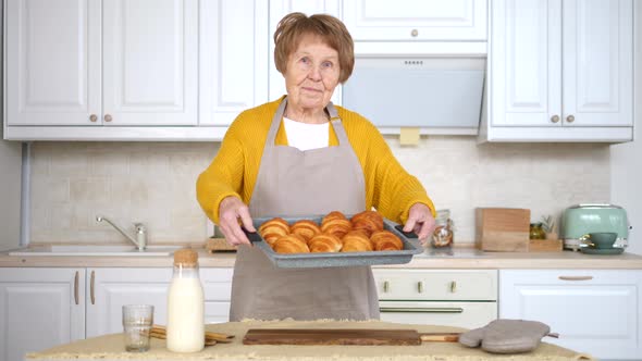 Elderly Woman Holding Baking Tray With Pastry. Granny With Baked Croissants. alt