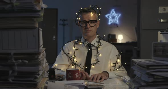 Sad corporate businessman working on Christmas day, he is wrapped in Christmas lights