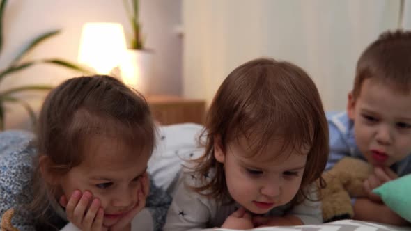 Smiling Preschool Toddler Children In Pajamas Watching Cartoon on Smartphone on Bed