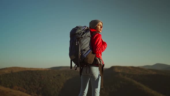 Woman Traveler with a Backpack Stands on a Rocky Hill and Looks at the Mountain Landscape on a alt