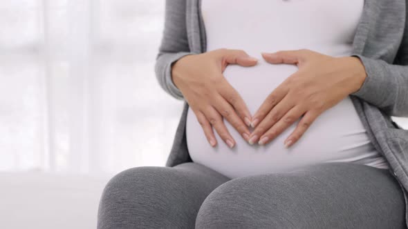 Dolly Shot Hand of pregnant woman make heart sign on her bare belly. alt