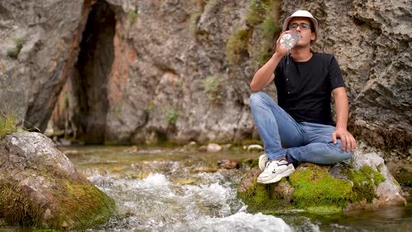 Man takes and drinks water from a mountain stream alt