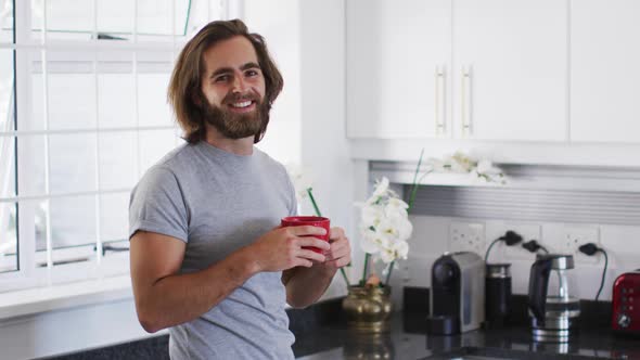 Portrait of caucasian man holding coffee cup and smiling in the kitchen at home alt