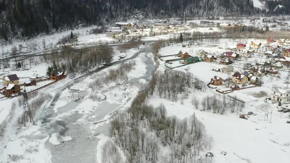 Aerial view of a Mountain Village with Hills Covered in Snow and Pine Forest in Winter