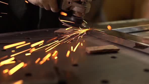 Male Worker Polishing Metal Part With Grinder. Sparks Fly Into the Camera. Slow Motion