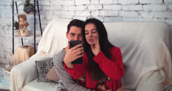 Young Couple Using Smart Phone Talking To Family Congratulates Merry Christmas By Video Call alt