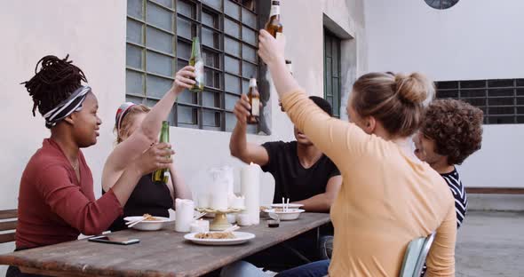 Slow motion shot of friends toasting with beer bottles during lunch alt
