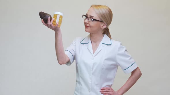Nutritionist Doctor Holding Organic Avocado Fruit and Jar of Medicine or Vitamin or Omega 3 Capsules alt