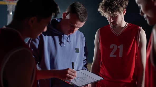 International Basketball Game the Coach Instructs Team Players on the Tactics of Game Using a Tablet alt
