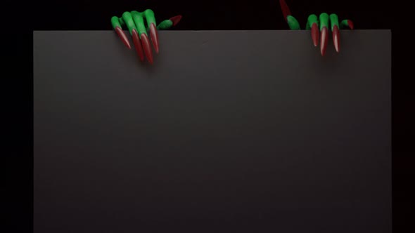 Green Witches Hands Appears From Behind a Black Background with Copyspace