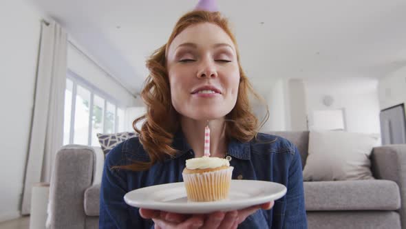 Portrait of woman in party hat blowing candle on the cake alt