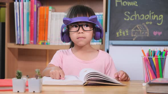 Cute little girl with headphones listening to audiobooks and looking at books at home. alt