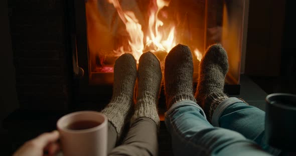 Couple Warm Up Feet in Woolen Socks By Fireplace Flame Drinking Tea in Cozy Room