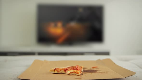 Man Throws a Piece of Halfeaten Pizza on the Sofa in Front of the TV alt
