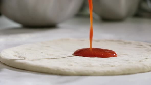 chef spreads tomato sauce from ladle dough. process of making pizza in pizzeria