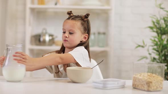 Child Pours Milk Into a Bowl of Cereal in the Kitchen.