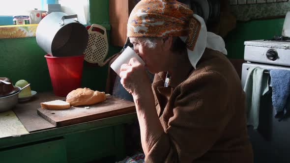 Sad Wrinkled Woman Drinks Tea From Cup and Chewing Food in Loneliness