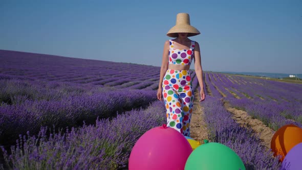 Woman in a Multicolored Suit with Circles and a Hat Holds Large Inflatable alt