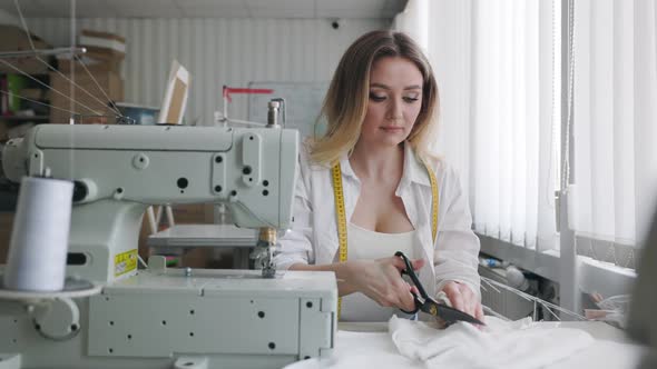 Young Beautiful Light Hair Seamstress Cuts Fabric in the Workplace