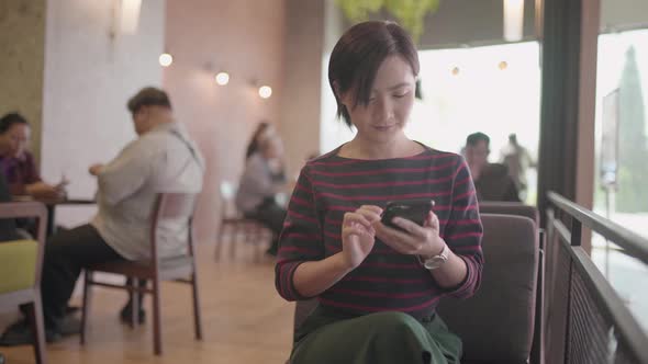 Happy asian woman using smartphone in cafe