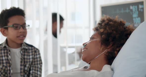 Preteen Afroamerican Son Visiting Sick Mother in Hospital and Talking alt