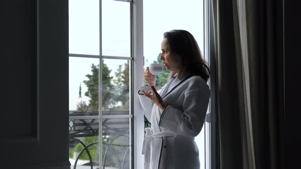 Woman in Bathrobe Drinking Coffee at Hotel Room alt