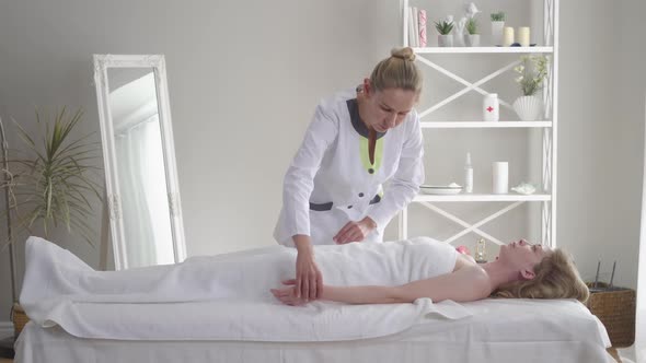 Confident Doctor Taking Pulse of Young Caucasian Woman Lying on Couch. Portrait of Professional alt