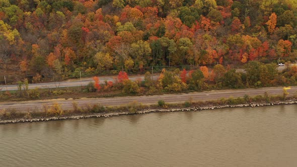 aerial shot over the Hudson River, while the camera trucks right, focusing on the autumn colored tre alt