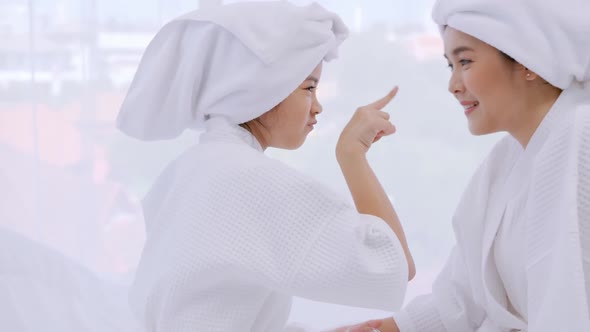 Mother with little daughter in bathrobes doing beauty treatment together at home. alt