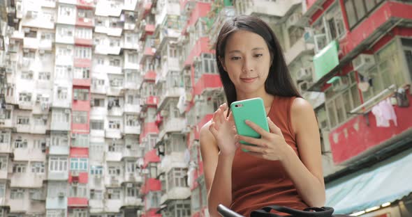 Woman using mobile phone in residential building in Hong Kong city alt