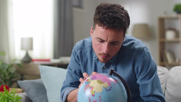 Young Man Looking for Country on Globe at Home in Living Room alt