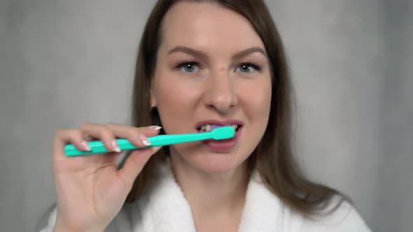 Woman in White Bathrobe Cleans Her Teeth with Toothbrush and Paste After Shower
