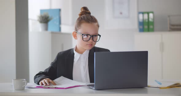 Concentrated Little Girl Boss Working on Laptop and Doing Paperwork in Office alt