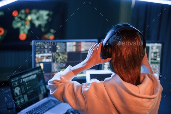 A lot of information on displays. Young professional female hacker is indoors by computer