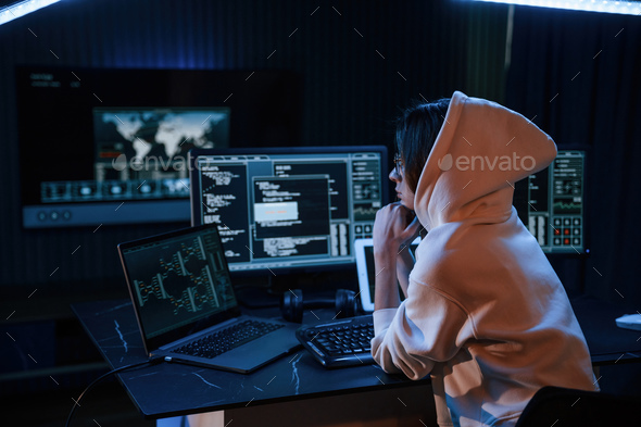 Young professional female hacker is indoors by computer with lot of information on displays