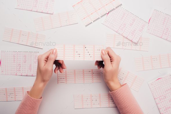 cropped view of woman holding lottery ticket with marked numbers near scattered lottery cards on