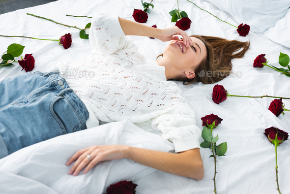 smiling woman obscuring face and lying on bed with roses