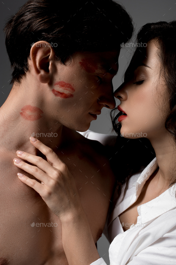 seductive woman hugging man with red lipstick prints, isolated on grey