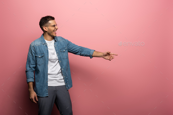 Side view of laughing man pointing with finger on pink background