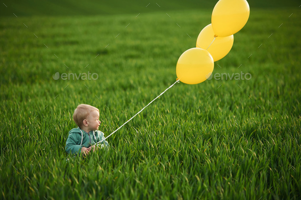 With yellow balloons in hands. Cute little baby boy is in the ...