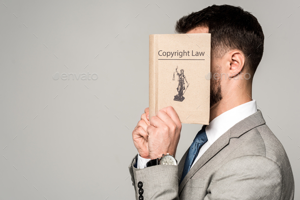 side view of lawyer obscuring face with copyright law book isolated on grey - Stock Photo - Images